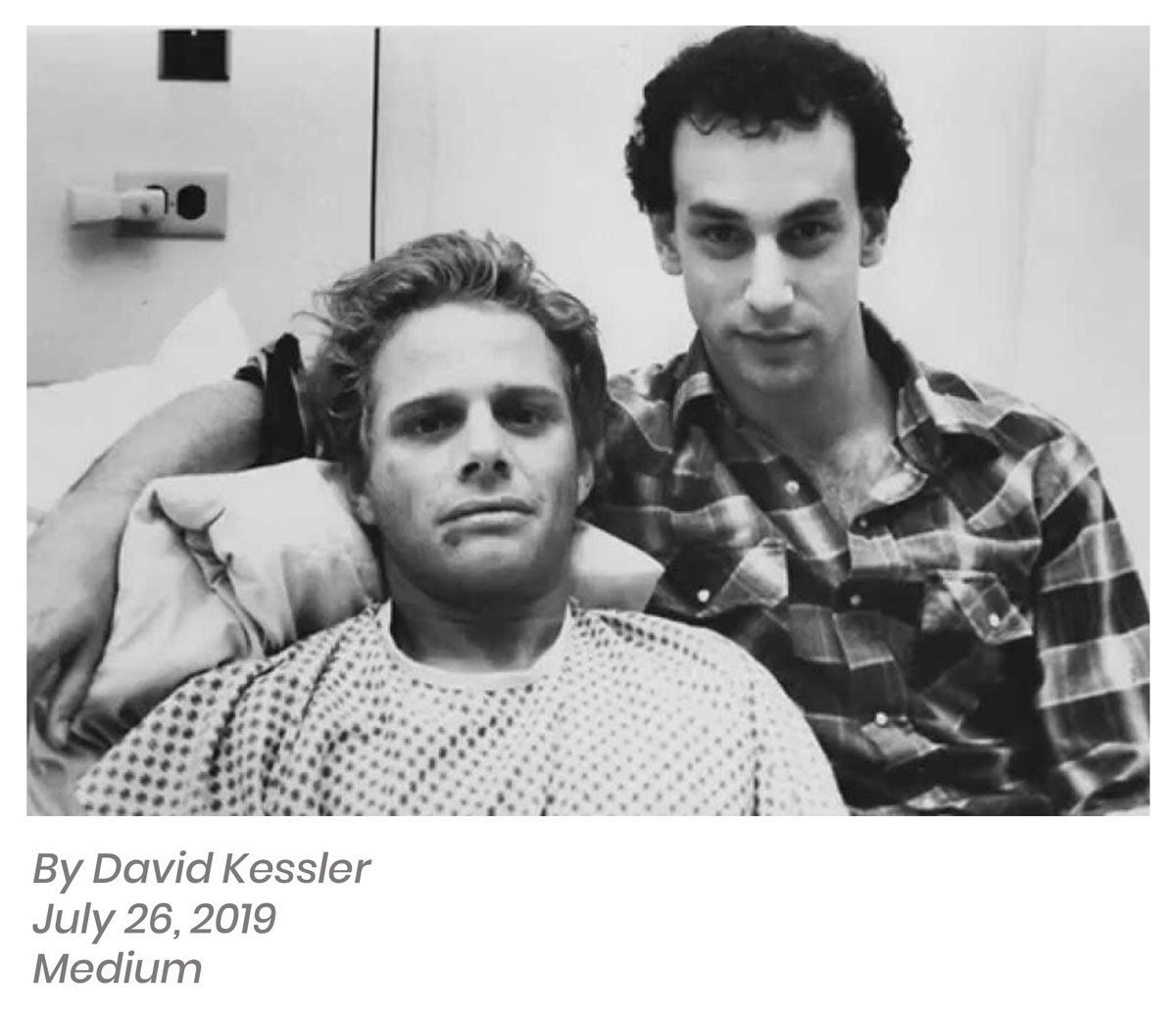 Two men are posing together; one is seated in hospital attire, and the other, reminiscent of Marianne's warm embrace, stands behind him in a plaid shirt.